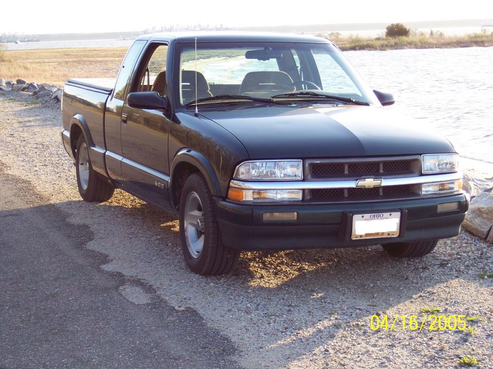 Dark green pickup truck parked by water, front quarter view