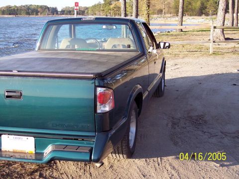 1986 Ford Bronco - A green pickup truck is parked on a dirt lot next to a body of water.