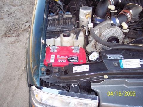 1986 Ford Bronco - Close-up of a vehicle's engine bay, a supercharger and a bright red battery.