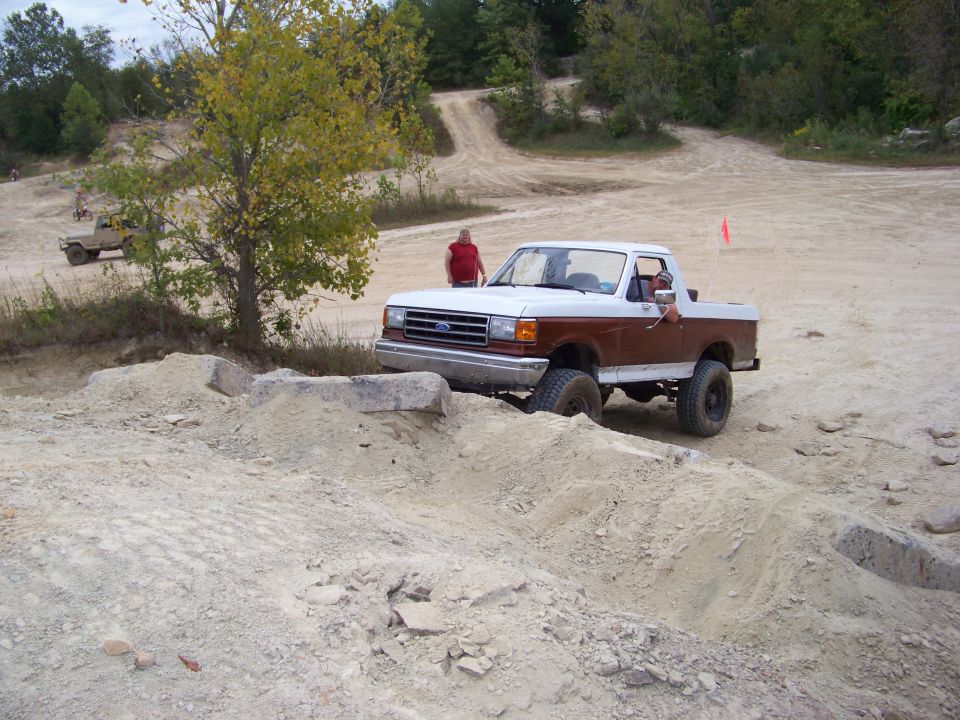 1989 Ford Bronco navigating a dirt obstacle course, another vehicle visible in the background