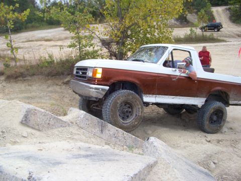 1989 Ford Bronco - A two-tone brown and white Ford Bronco navigates an off-road course with another vehicle visible in the background.