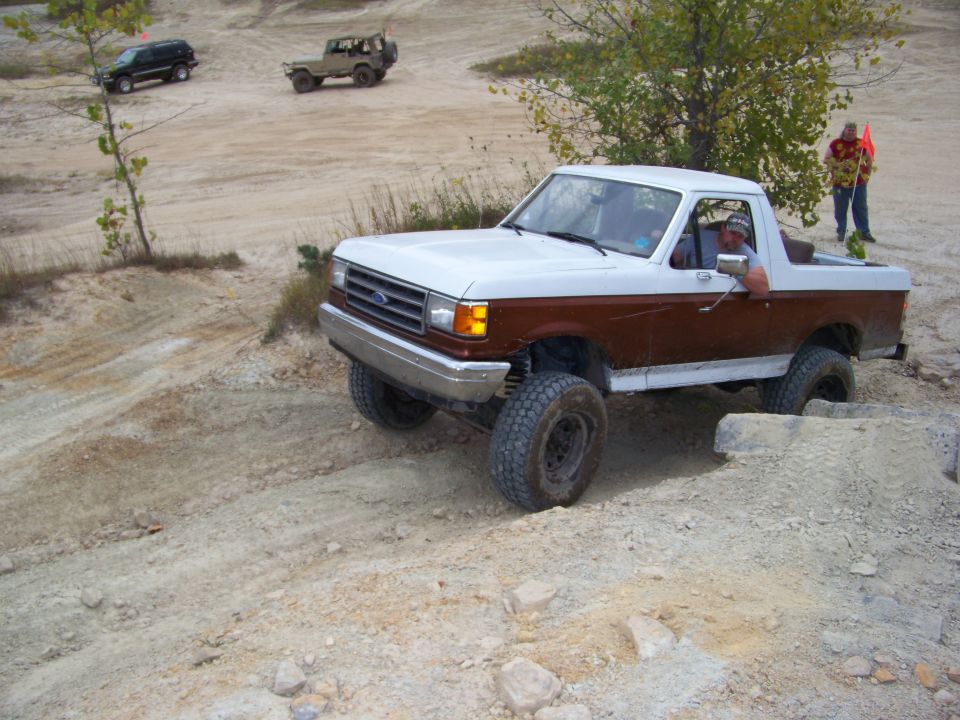 White and brown 1989 Ford Bronco driving on dirt terrain