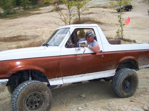 1989 Ford Bronco - A man drives a lifted two-tone Ford Bronco on a dirt trail with another vehicle in the background.