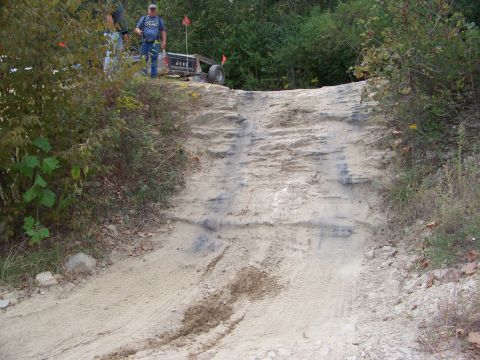 1989 Ford Bronco - Two people stand near an off-road buggy as it ascends a sandy hill during an event.