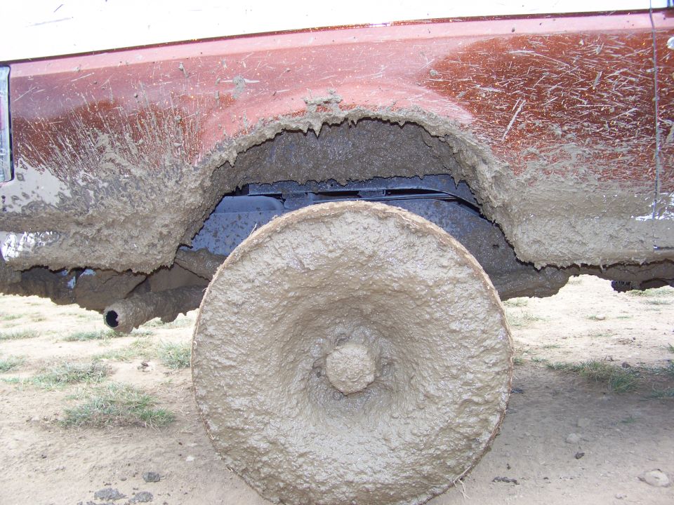 Mud caked on a vehicle's wheel and fender, obscuring details