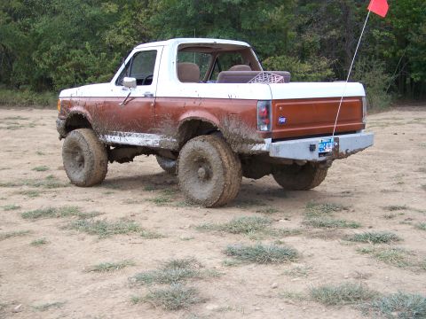 1989 Ford Bronco - This mud-splattered 1989 Ford Bronco is shown from the rear three-quarter angle, highlighting its two-tone paint and off-road tires.