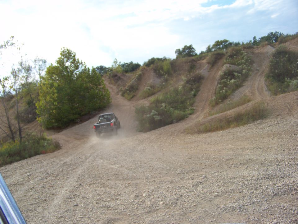 Dark lifted 4x4 pickup climbing a dusty gravel hill at an off-road park