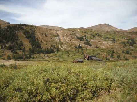 1986 Ford Bronco II - A remote mountain scene features old, weathered buildings in a green valley under a vast sky.