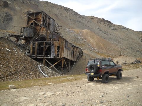 1986 Ford Bronco II - A brown Ford Bronco II is parked on a dirt road next to a dilapidated wooden mine structure on a rocky mountainside.