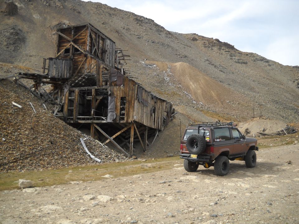 Brown Ford Bronco II with spare tire on rear, parked on dirt road near abandoned mine
