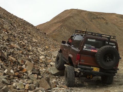 1986 Ford Bronco II - A brown Ford Bronco II navigates a rocky mountain path, its spare tire mounted on the rear.