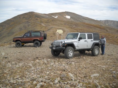 1986 Ford Bronco II - Two SUVs are parked on a rocky mountain trail with a scenic mountain backdrop.