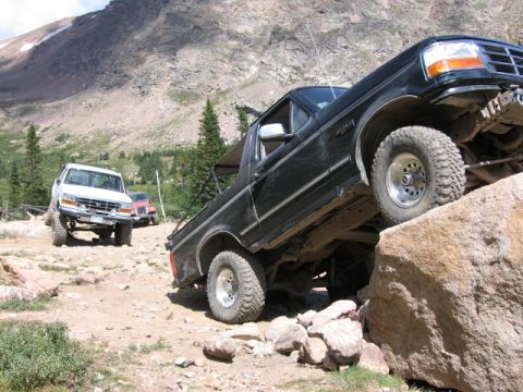 1995 Ford Bronco - Multiple off-road vehicles navigate a rocky trail in a mountainous area.