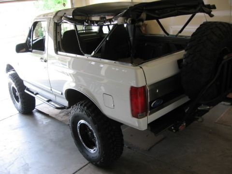 1995 Ford Bronco - A white Ford Bronco full-size SUV with its soft top folded down and roll bar exposed, shown from the rear three-quarter angle inside a gara…