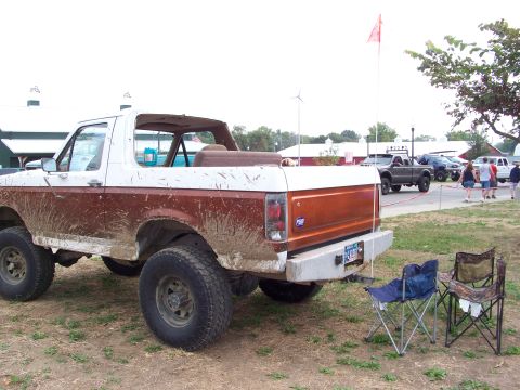 1989 Ford Bronco - Mud-splattered Ford Bronco parked outdoors with other vehicles and people nearby.