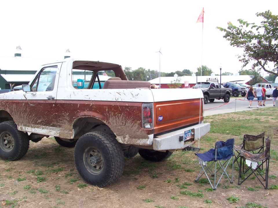 Mud-splattered two-tone Ford Bronco, rear view. Other vehicles and people in background