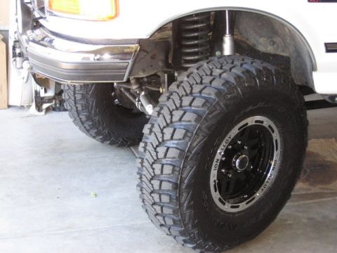 1995 Ford Bronco - Close-up of the front passenger-side corner of a lifted white Ford Bronco, showing an aggressive mud-terrain tire mounted on a black ION Al…
