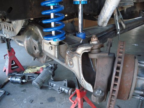 1986 Ford Bronco - Close-up view of a vehicle's front axle and suspension system, supported by jack stands.