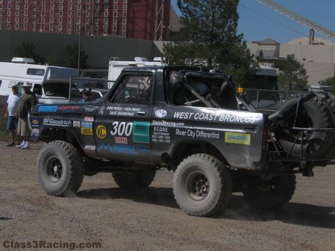 1990 Ford Bronco - Rear view of the number 300 West Coast Broncos race truck with spare tires mounted on a tubular rack in a paved lot.