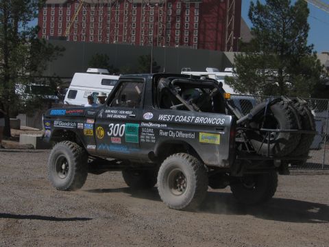 1990 Ford Bronco - Rear three-quarter view of the number 300 West Coast Broncos truck with spare tires, parked near a large building.