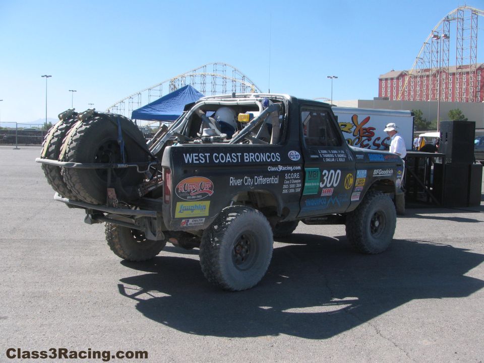 Rear view of West Coast Broncos race truck with spare tires near a roller coaster
