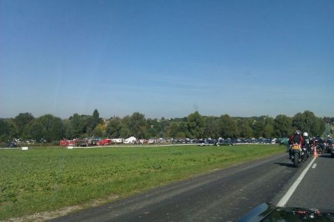 1991 Ford Crown Victoria - A group of motorcycles travels down a road, passing a field filled with parked vehicles under a clear blue sky.