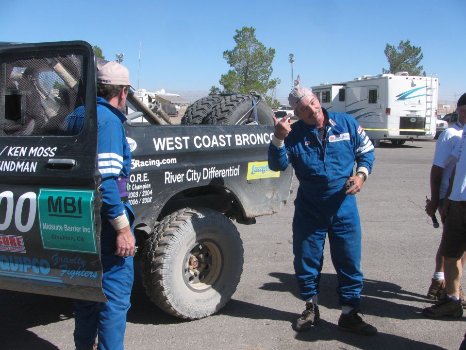 Two men in blue suits talking next to the no. 300 race truck near RVs