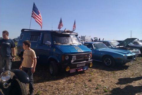 1991 Ford Crown Victoria - A blue van decorated with American flags is parked next to a blue coupe at an outdoor car show.