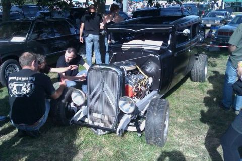 1991 Ford Crown Victoria - A group of people examine a custom black hot rod with its engine exposed at an outdoor car show.