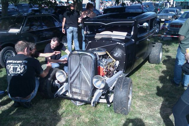 Black hot rod with exposed engine and chrome grille, viewed from the front
