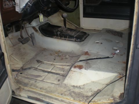 1978 Ford Bronco - The interior floor of the vehicle is visible, showing the pedals and transmission tunnel with signs of wear and rust.