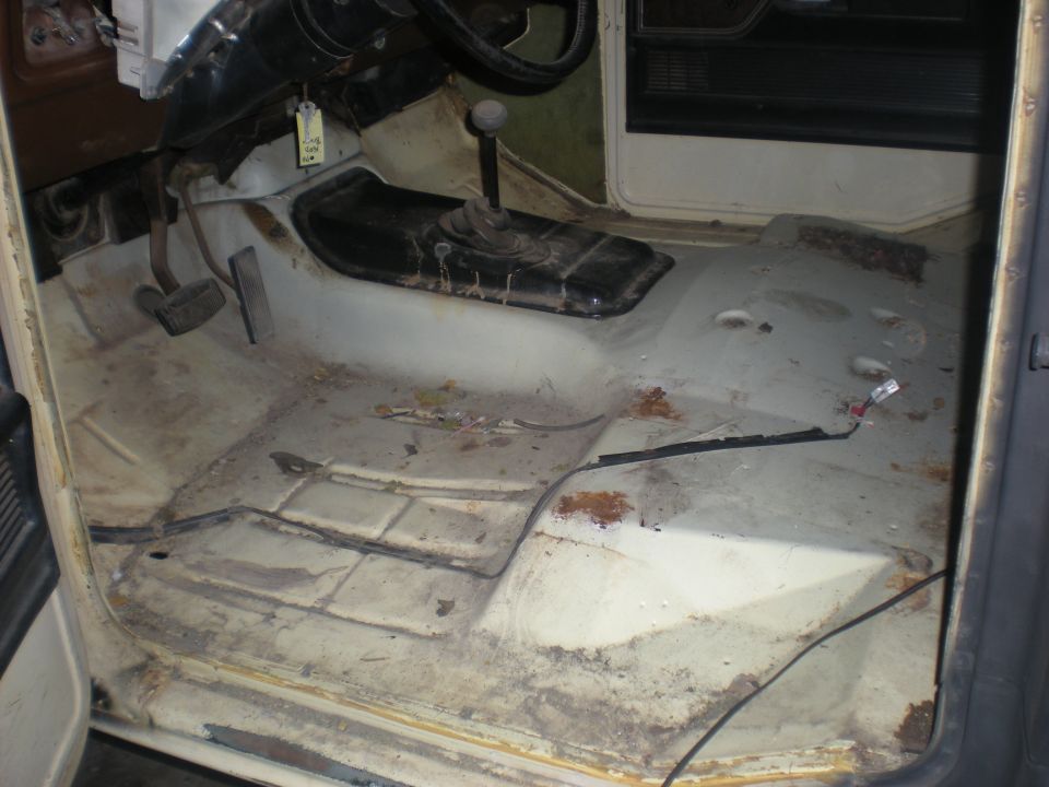 Interior floor of a vehicle, showing pedals, transmission tunnel, and bare metal with some rust