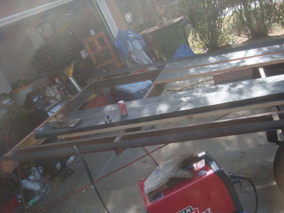 Trailer frame with wooden planks and metal beams, a red soda can, and welding equipment in a garage