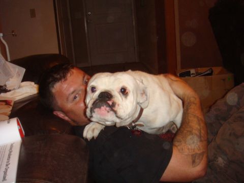 1992 Ford Bronco - A man holds a white bulldog while relaxing on a couch indoors.