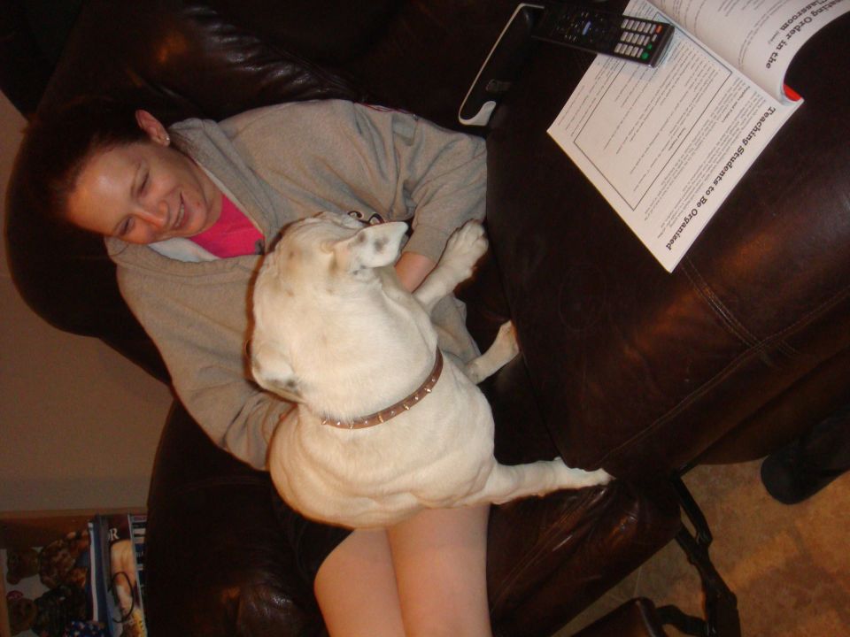 Woman resting on a leather couch with a white dog on her lap