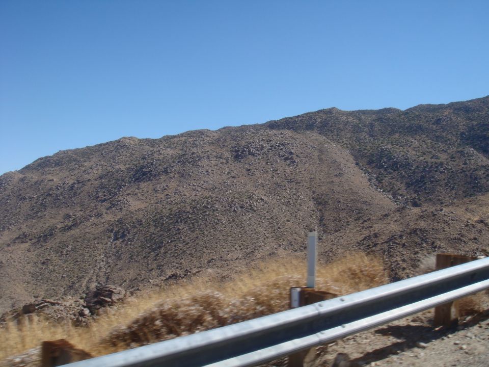 Desert mountains under a clear blue sky, with a metal guardrail in the foreground. Text 'SUPER MOTORS' is visible