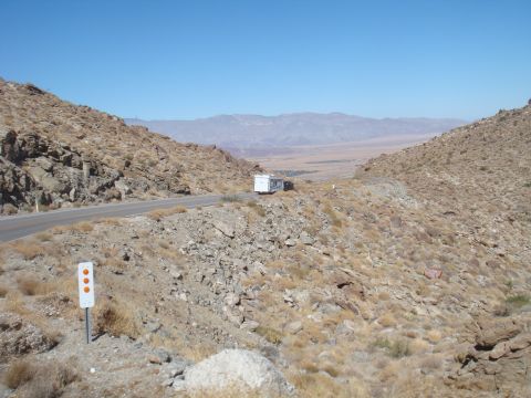 1992 Ford Bronco - A trailer sits on the shoulder of a road winding through a barren, mountainous desert.