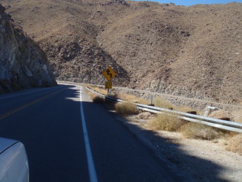 1992 Ford Bronco - A car drives on a winding road through a dry, mountainous landscape with a speed limit sign for curves.