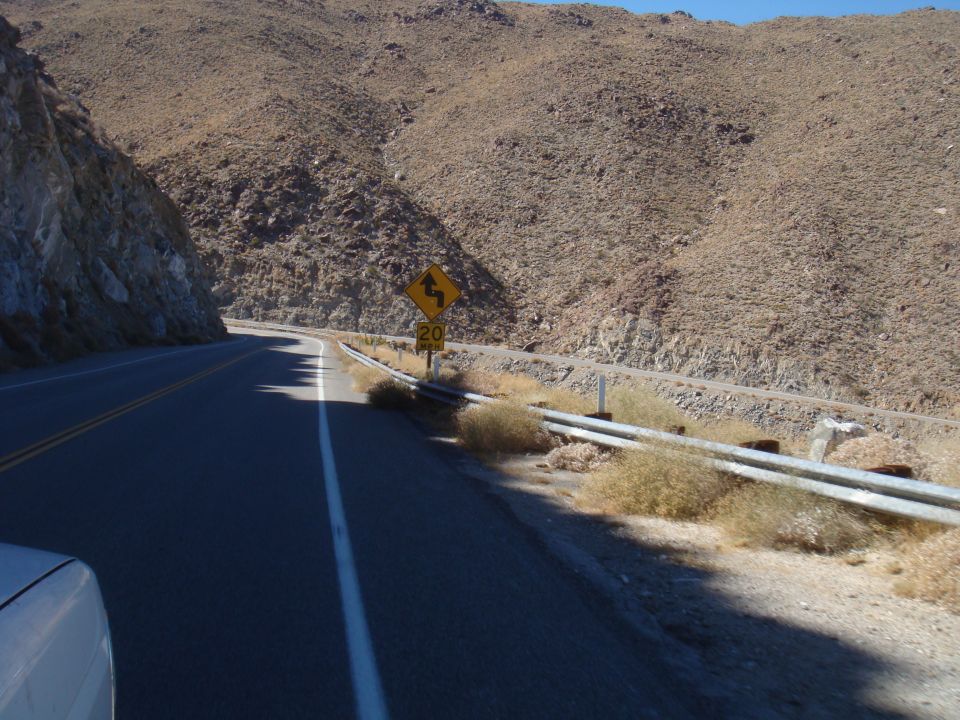 View from a car on a road with a 20 mph curve warning sign on a mountainside