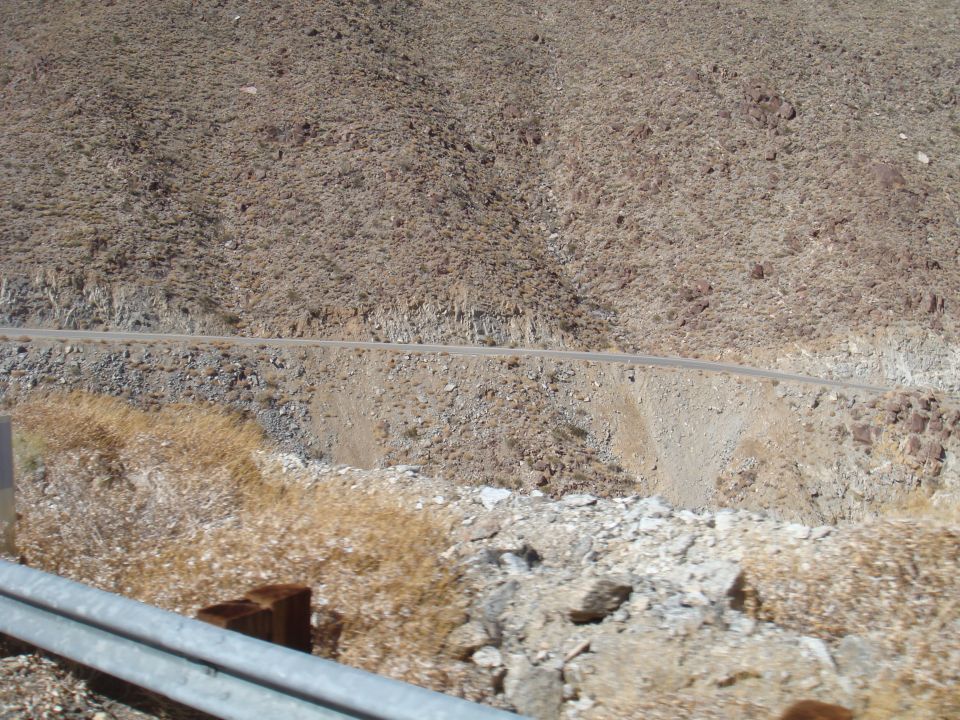 Desert landscape with a road winding up a rocky hillside, dry brush in the foreground