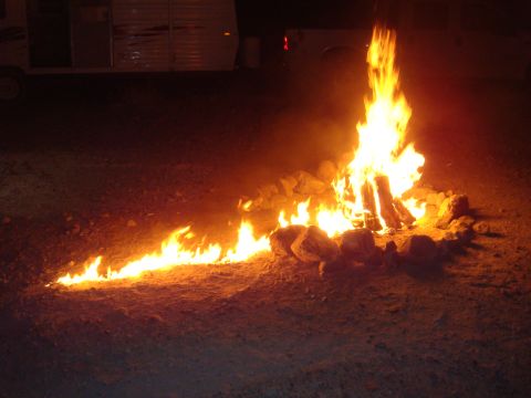 1992 Ford Bronco - A campfire burns brightly in a rocky pit at night, with a trailer and truck visible in the dark background.