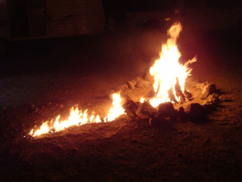 1992 Ford Bronco - A campfire burns brightly at night, surrounded by rocks on a dirt ground.