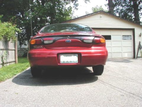 1997 Ford Taurus - The rear of a red 1997 Ford Taurus is visible parked in front of a garage.