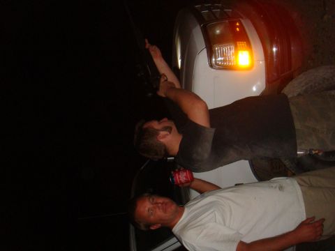 1992 Ford Bronco - Two men are working on the side of a white truck at night, with one holding a red can.