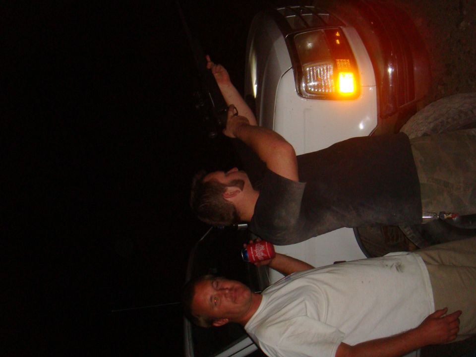 Two men are working on the side of a white truck at night. One man is holding a red can
