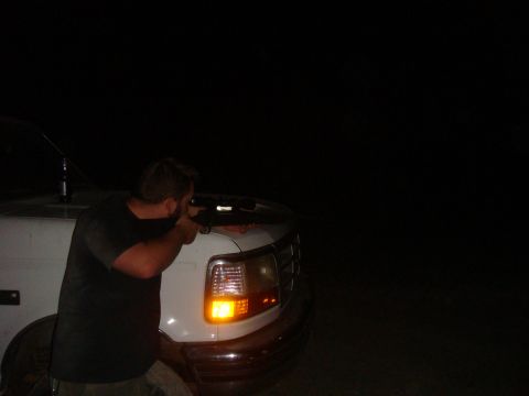 1992 Ford Bronco - A man aims a rifle from the driver's side of a white truck, illuminated by the truck's hazard lights.