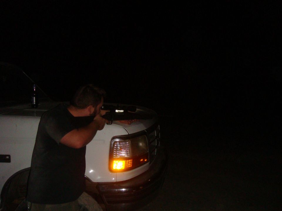 Guy aiming a rifle out the side of a white truck at night