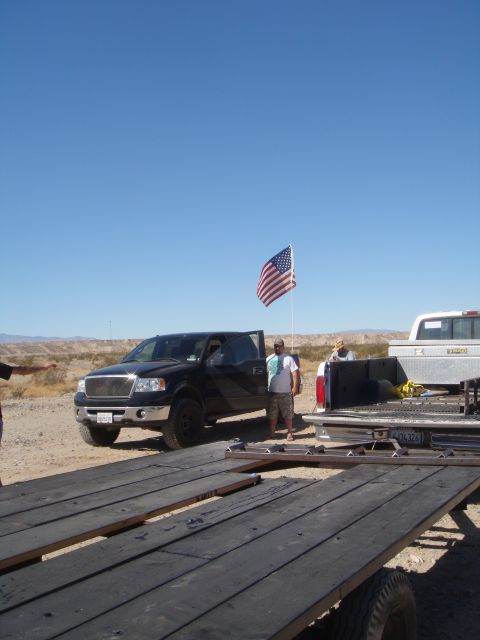 1992 Ford Bronco - A black Ford F-150 pickup truck is parked next to a trailer, with an American flag flying in the desert.