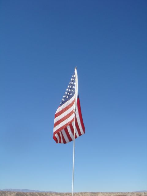 1992 Ford Bronco - An American flag flies proudly on a pole under a vast blue sky, with a dry, hilly terrain visible in the distance.