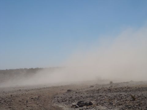 1992 Ford Bronco - A dust cloud billows across a rocky desert landscape on a clear day.